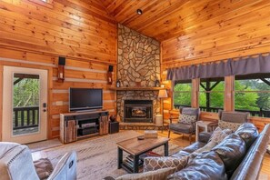 A log cabin interior with a stone fireplace, a television, and a sofa. - About Time - Year Round Mtn Views | Game Room | Hot Tub | Near Boone & Blowing Rock (Vilas)