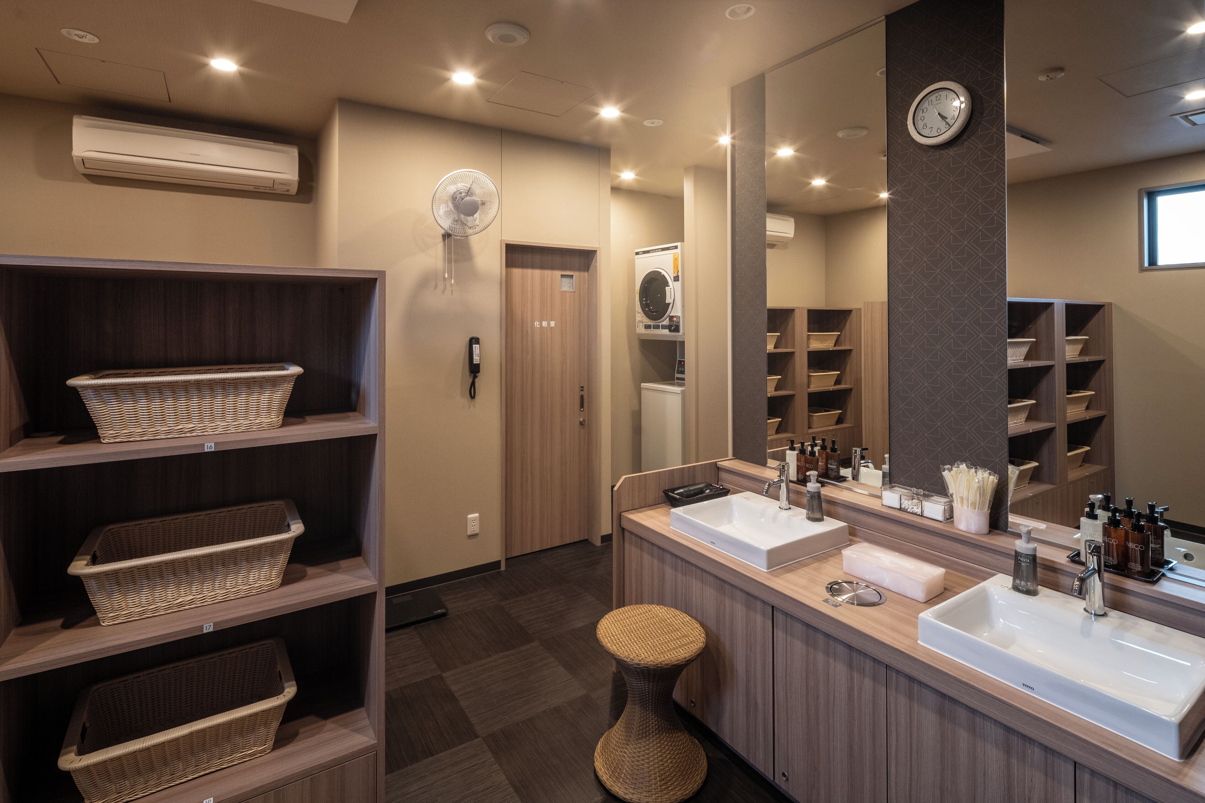 A modern bathroom with two sinks, a large mirror, and wicker baskets on shelves.