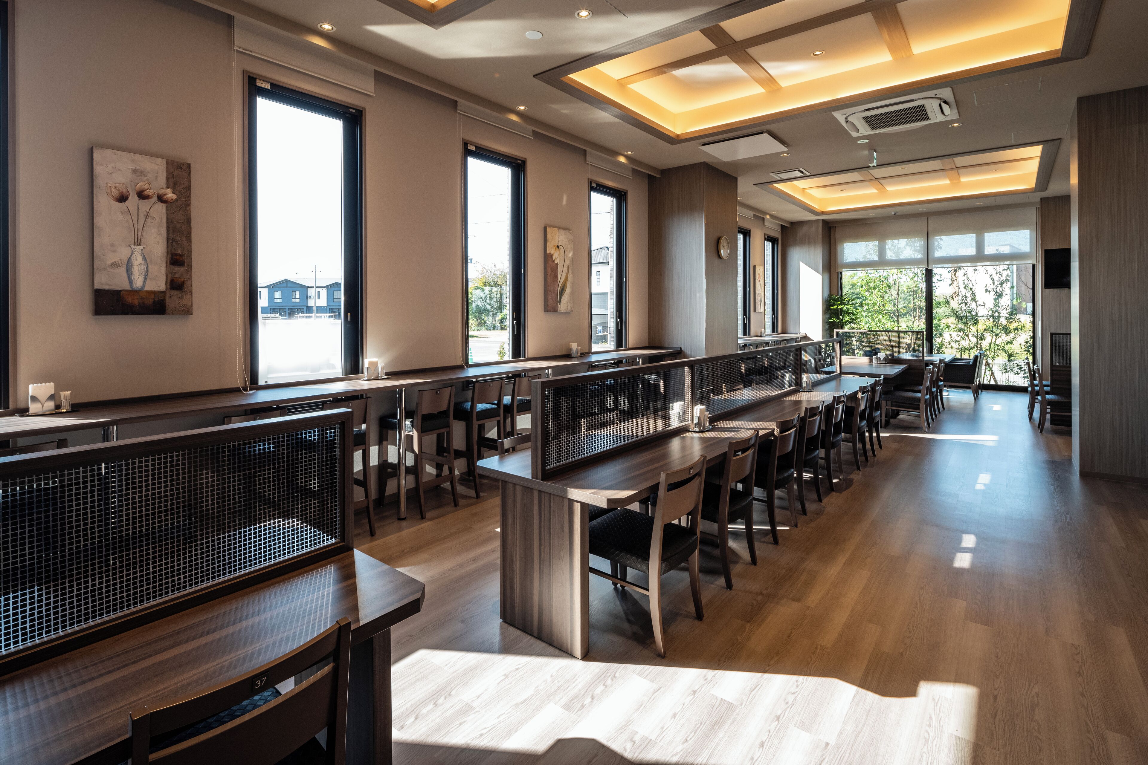 A spacious dining area with long tables and chairs, large windows providing natural light, and artwork on the walls.