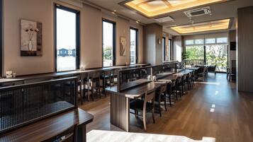 Un comedor amplio con mesas y sillas largas, ventanas grandes que proporcionan luz natural, y obras de arte en las paredes.