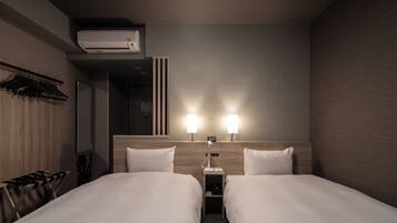 Habitación de hotel con dos camas, una mesita de noche con lámpara y aire acondicionado instalado en la pared.