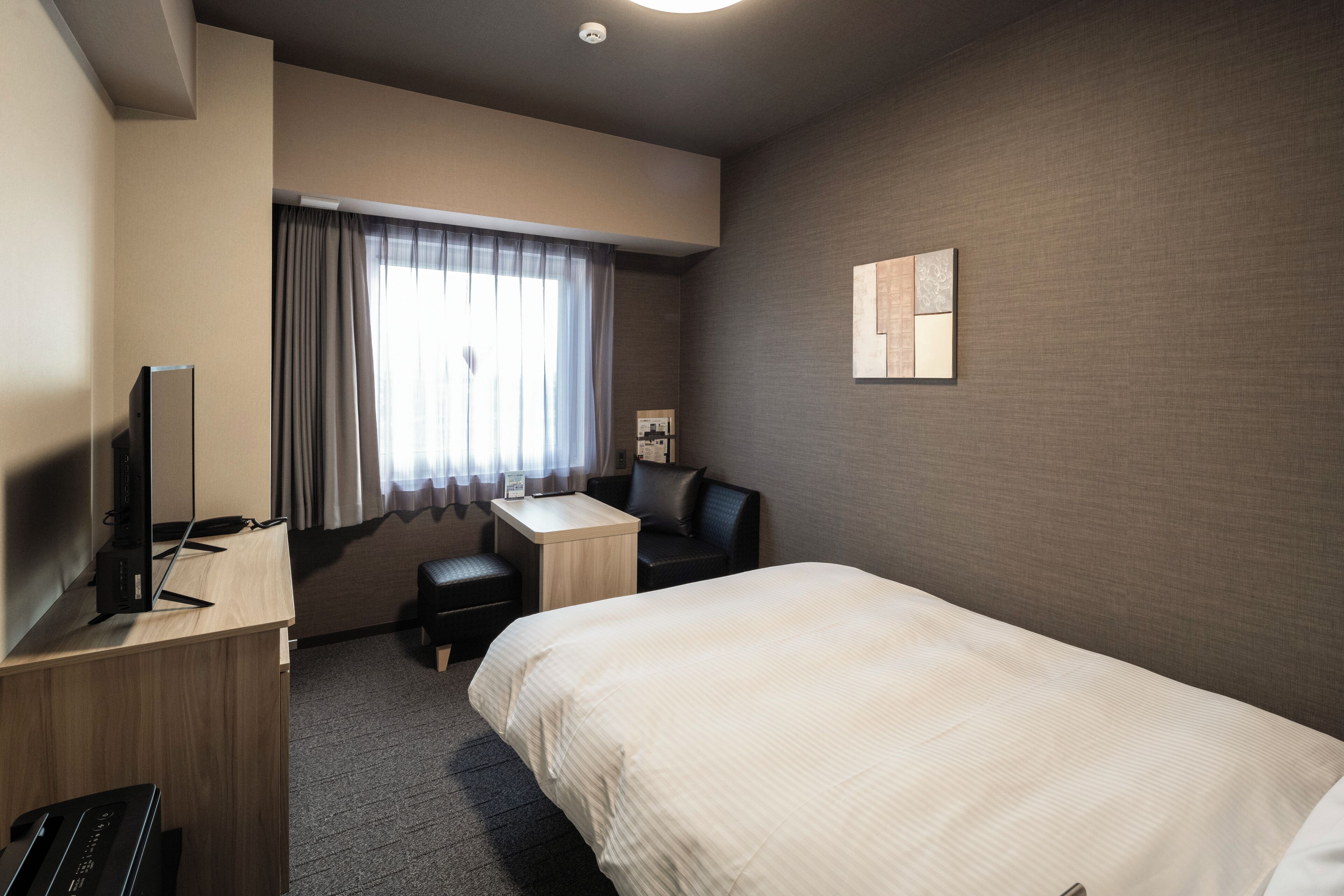A hotel room with a bed, a desk, a chair, a television, and a window with curtains.