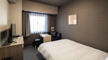 Habitación de hotel con cama, escritorio, silla, televisor y ventana con cortinas.