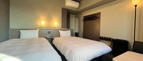 Ein Hotelzimmer mit zwei Betten, einem Schreibtisch, einer Lampe, einer Klimaanlage und einer Heizung.