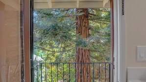 A view through a glass door with a metal railing, leading to a wooden tree trunk and surrounding greenery. - 2bed Apartment just 3 blocks from Downtown Martinez and Jobs (Martinez)