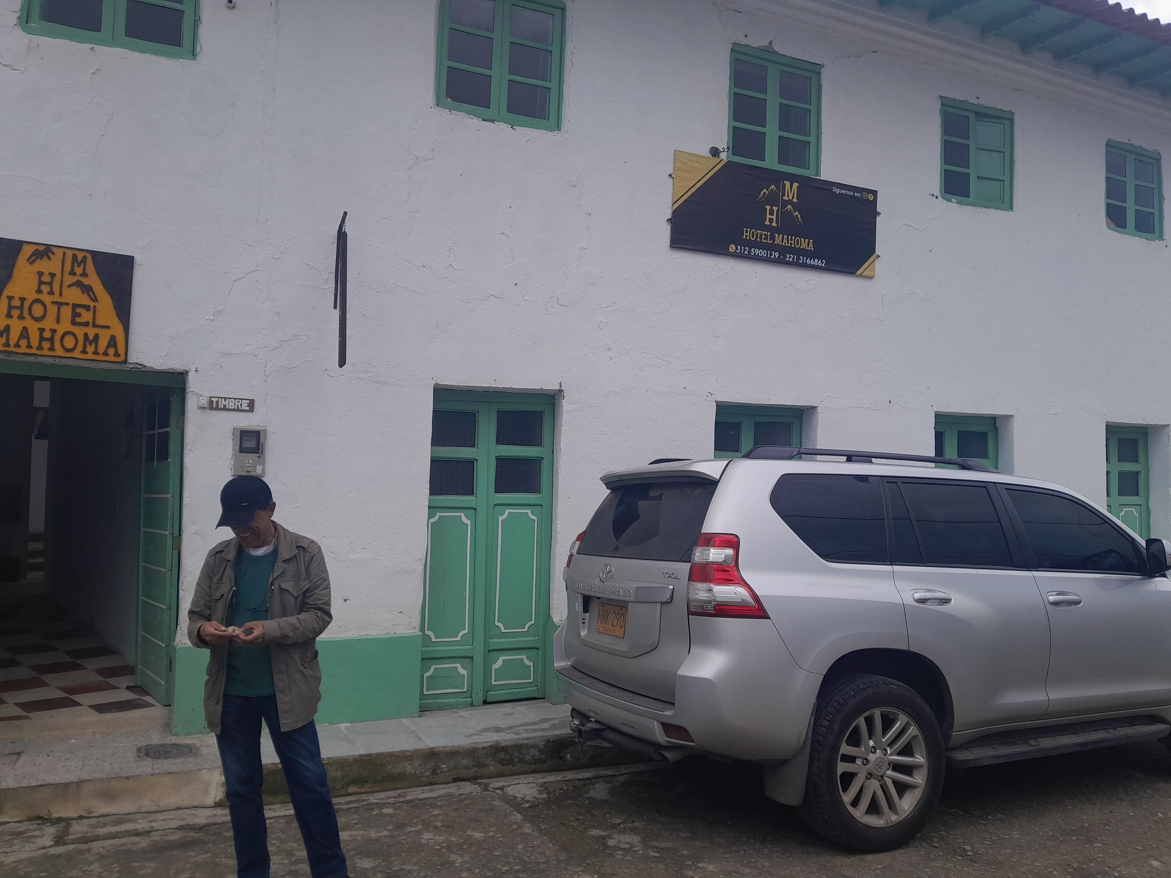 A building with a sign for Hotel Mahoma, a parked SUV, and a man standing in front.