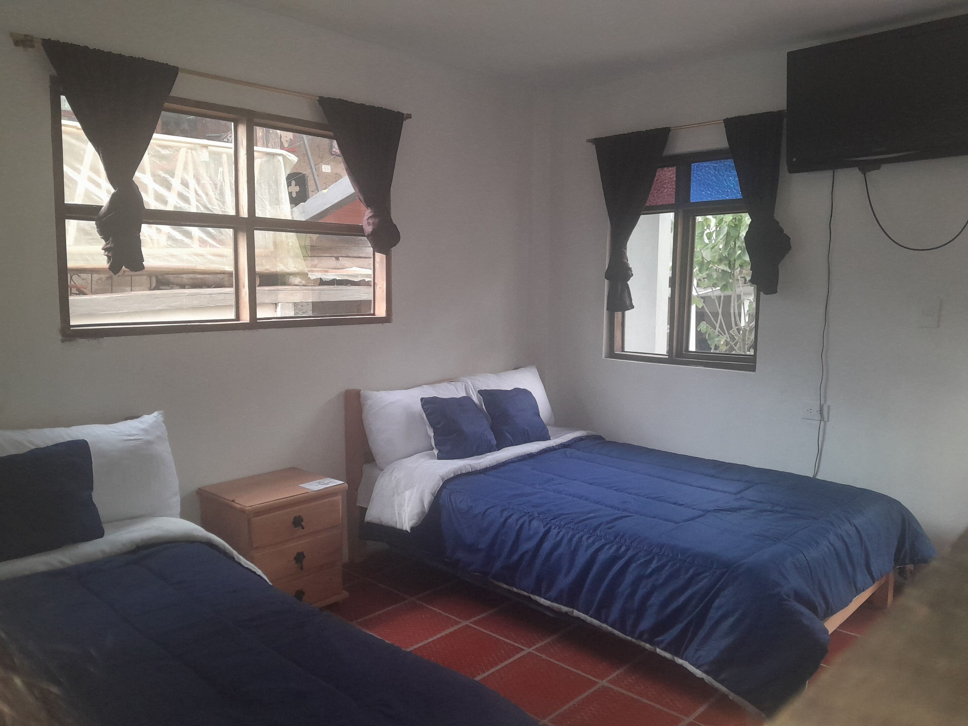 A bedroom with two beds, a nightstand, and a TV mounted on the wall.