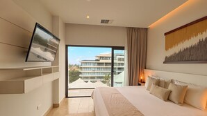 Une chambre d’hôtel moderne avec un grand lit, un téléviseur à écran plat fixé au mur, une vue sur la ville à travers la porte vitrée et un tableau au-dessus du lit.