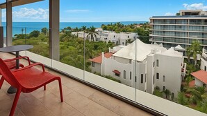 Un balcon avec une chaise rouge, une petite table et une vue sur l’océan et les bâtiments.