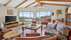 Un soggiorno spazioso con una grande TV, posti a sedere confortevoli e ampie finestre con vista sul mare.