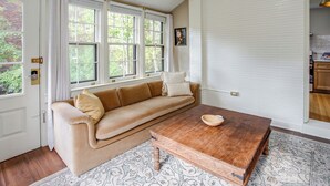 Ein Zimmer mit einem beigen Sofa, einem Holztisch und einem gemusterten Teppich.