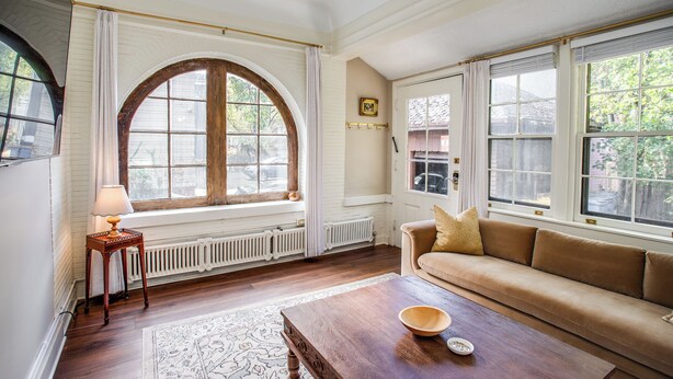 Ein Wohnzimmer mit einer Couch, einem Couchtisch, einer Lampe und großen Fenstern.