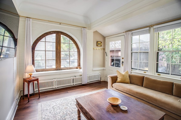 A living room with a sofa, a coffee table, a lamp, and large windows.