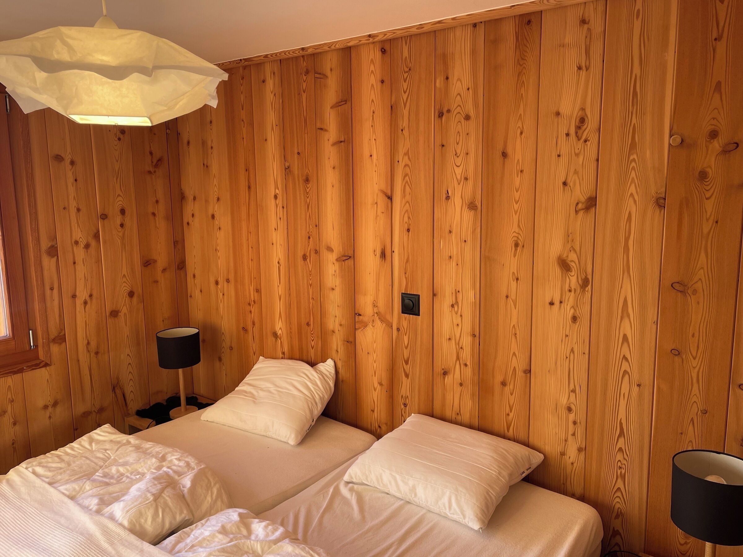 Ein Zimmer mit Holzwandverkleidung, einem Bett mit weißer Bettwäsche, einer Nachttischlampe und einer Hängelampe.