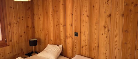 A room with wooden panel walls, a bed with white bedding, a bedside lamp, and a hanging light fixture.