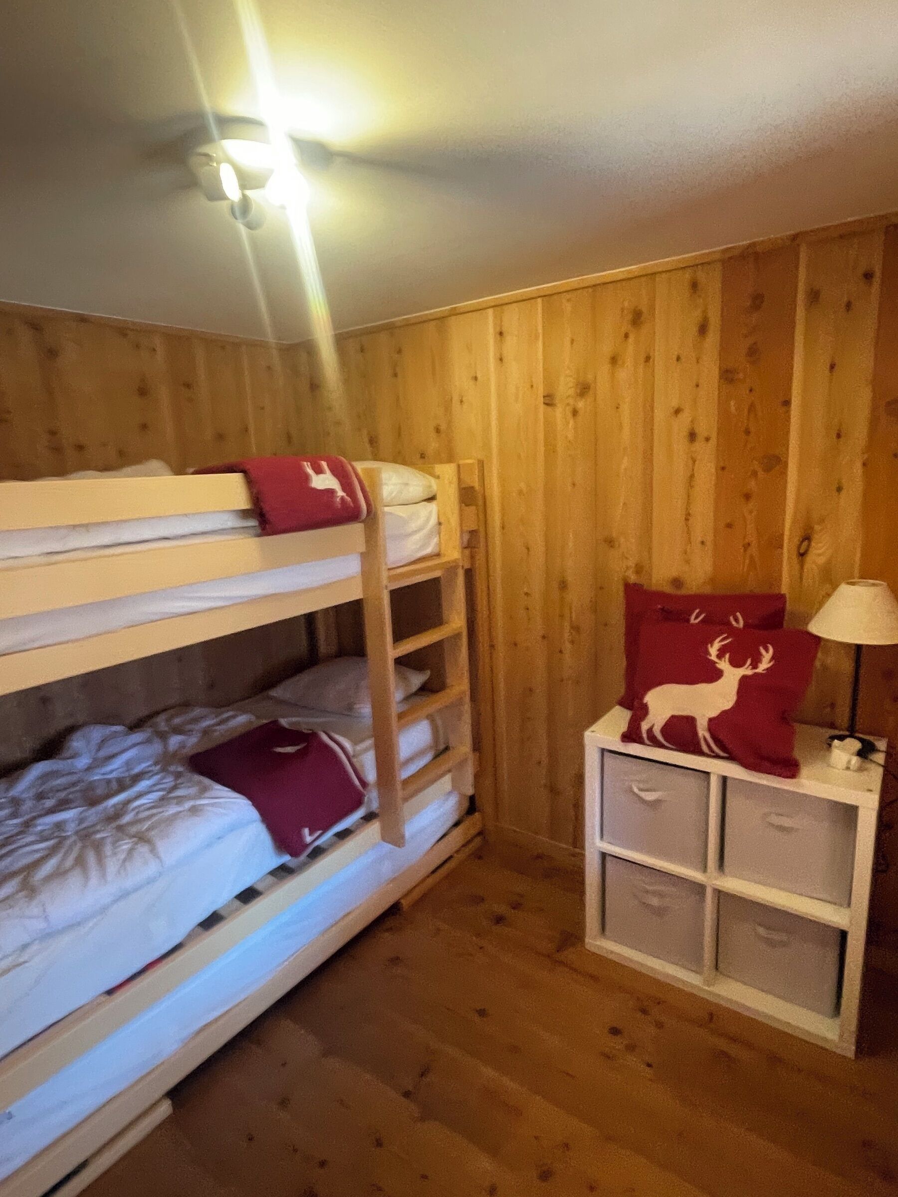 Habitación con literas, paredes de madera y una mesita de noche pequeña con cajones.