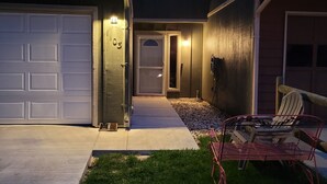 Une maison d’habitation avec un garage, une porte d’entrée et un petit patio comprenant une chaise et une table.