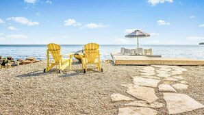 A pebble beach with two Adirondack chairs and a table under a beach umbrella, overlooking the sea. - Lake Simcoe Luxury Cottage | Sauna + Hot Tub (Brechin)
