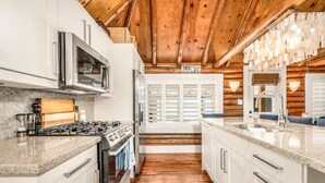 A modern kitchen with white cabinetry, a stainless steel range, and a wooden ceiling. - Lake Simcoe Luxury Cottage | Sauna + Hot Tub (Brechin)