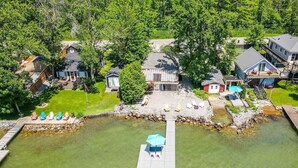 An aerial view of a lakeside property with a dock, a small house, and a larger building with a deck. - Lake Simcoe Luxury Cottage | Sauna + Hot Tub (Brechin)