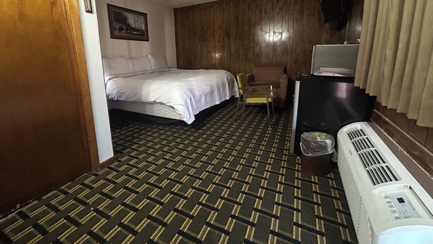 A hotel room with a bed, a chair, a desk, and a heater. - Big 12 Motel Broken Bow Ne (Broken Bow)