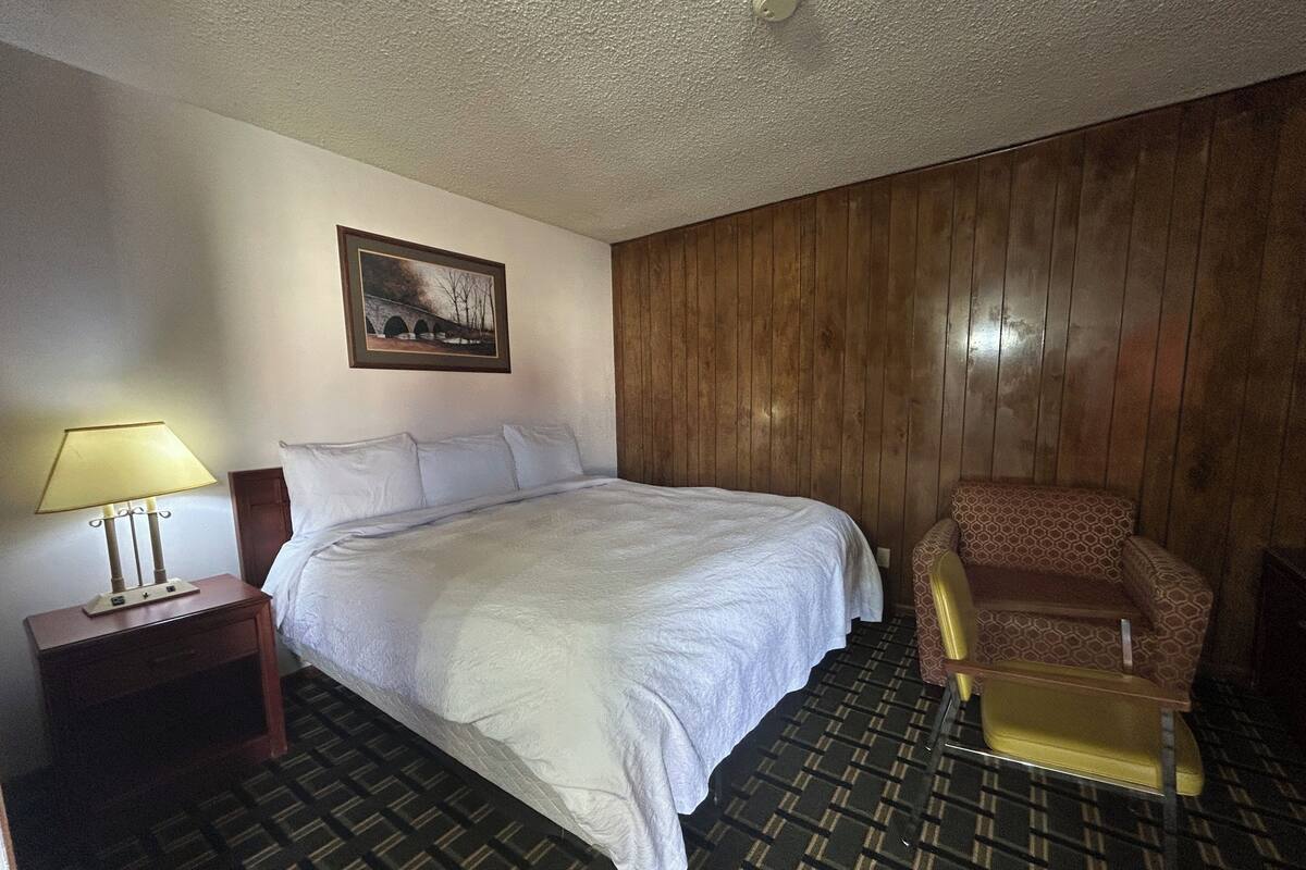 Een hotelkamer met een bed, een stoel, een nachtkastje met een lamp en een schilderij aan de muur.