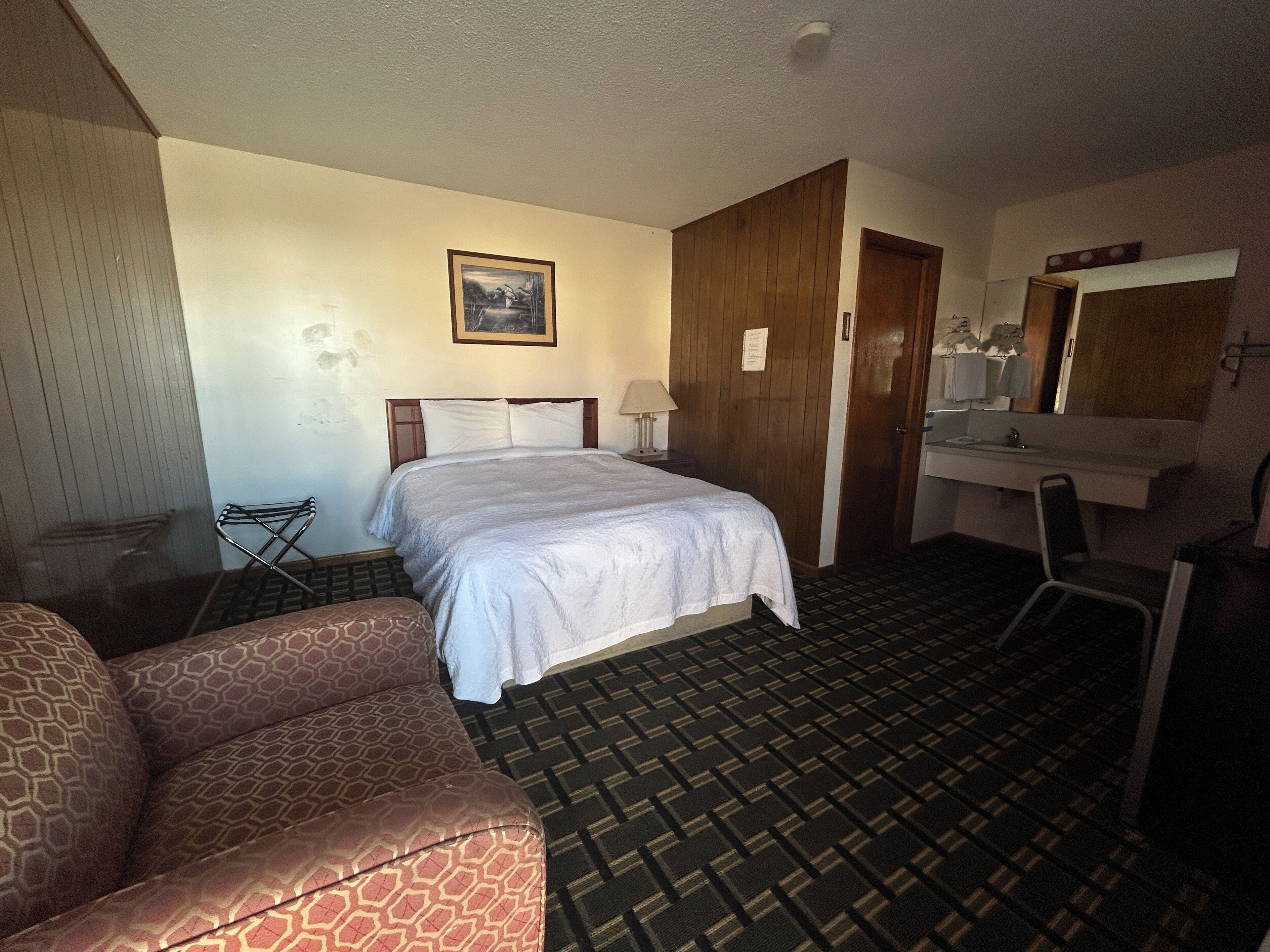 Una camera d'albergo con un letto, una sedia, una scrivania, uno specchio e un bagno.