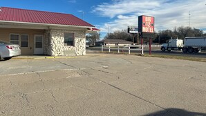 A motel with a stone facade, a red roof, and a sign advertising rooms starting at $22. - Big 12 Motel Broken Bow Ne (Broken Bow)