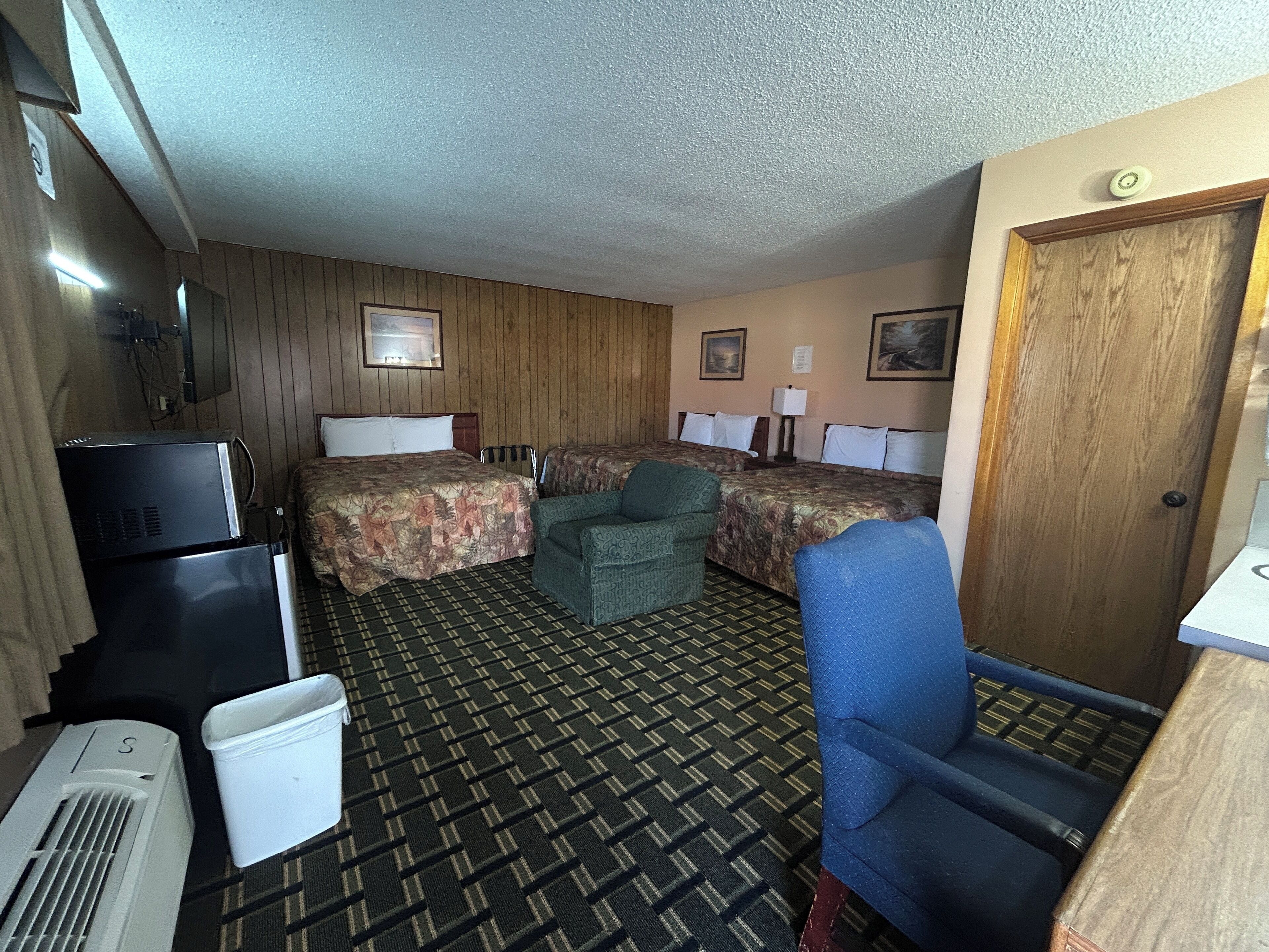 A hotel room with two beds, a desk, a chair, a TV, and a trash bin.