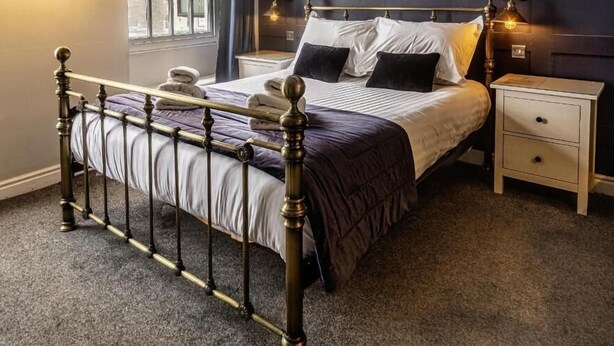 Quarto com cama de dossel, mesa de cabeceira, cômoda e janela com cortinas.