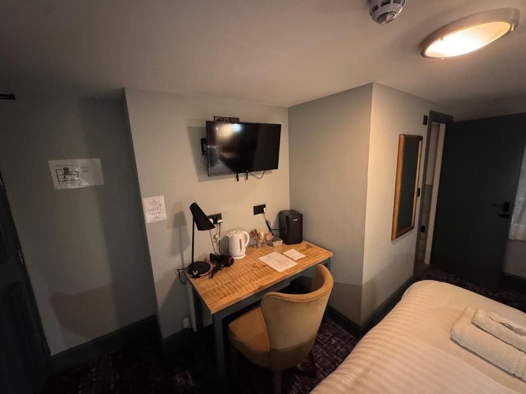 A hotel room with a bed, a desk with a chair, a television, and a door.