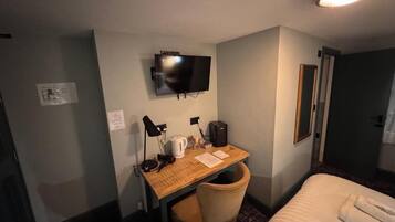 A hotel room with a bed, a desk with a chair, a television, and a door.