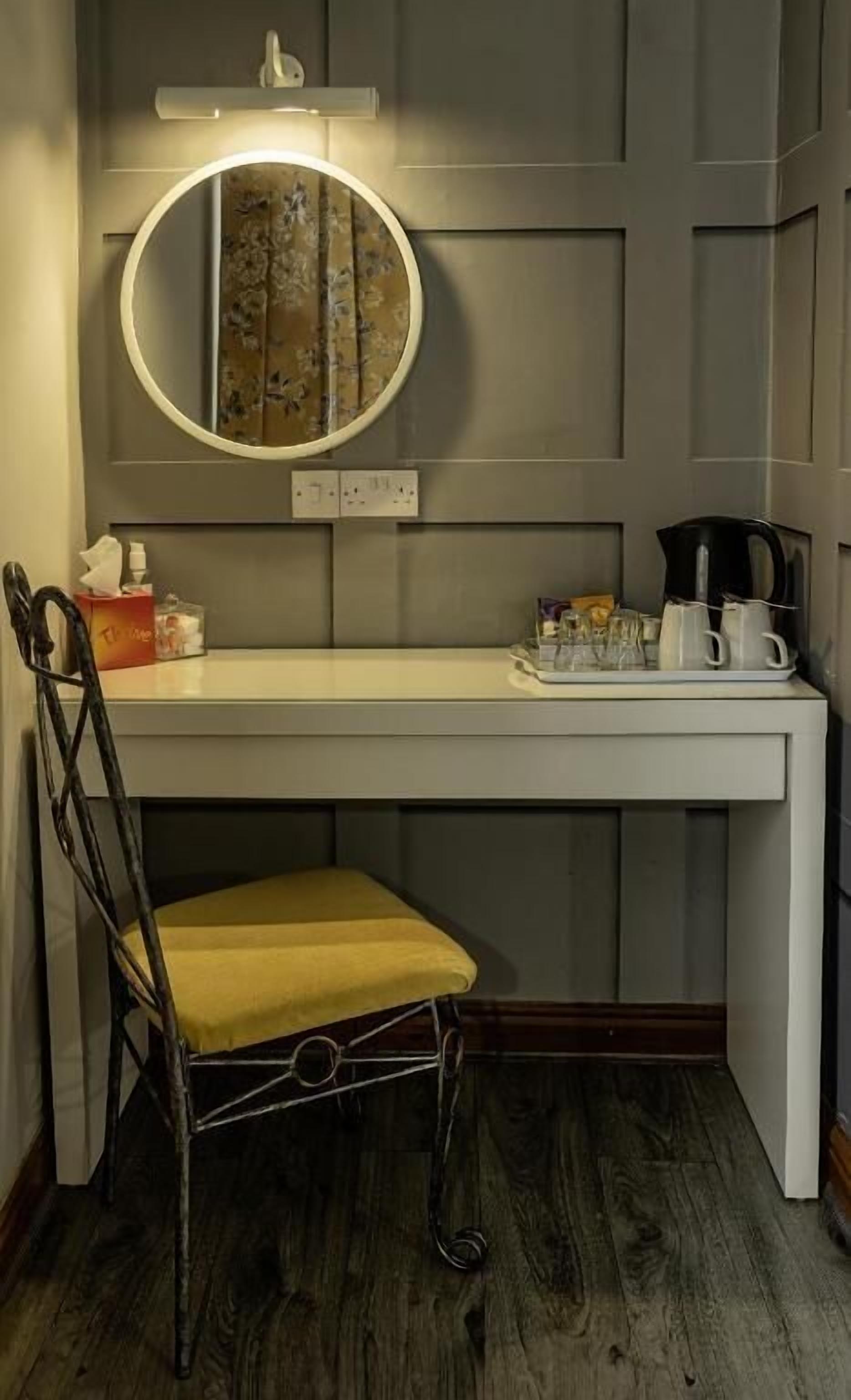 A small desk with a round mirror, a chair, and a coffee maker.