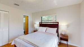 A bedroom with a large bed, two bedside tables with lamps, a window with blinds, and a door leading to another room. - Serenity House — Sunny Private Pool Escape, Dog-Friendly with BBQ Grill & Enclosed Yard 🌞 (Vero Beach)