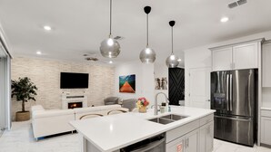 Une cuisine moderne dotée d’un îlot central, d’appareils électroménagers en acier inoxydable et de luminaires suspendus.