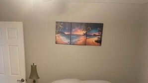 Ein Schlafzimmer mit einem Bett, einem Nachttisch, einer Lampe und einem Wandbild.
