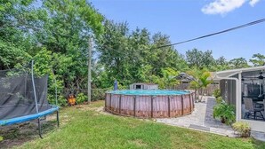 Ein Garten mit einem hölzernen Whirlpool, einem Trampolin und einer überdachten Terrasse.