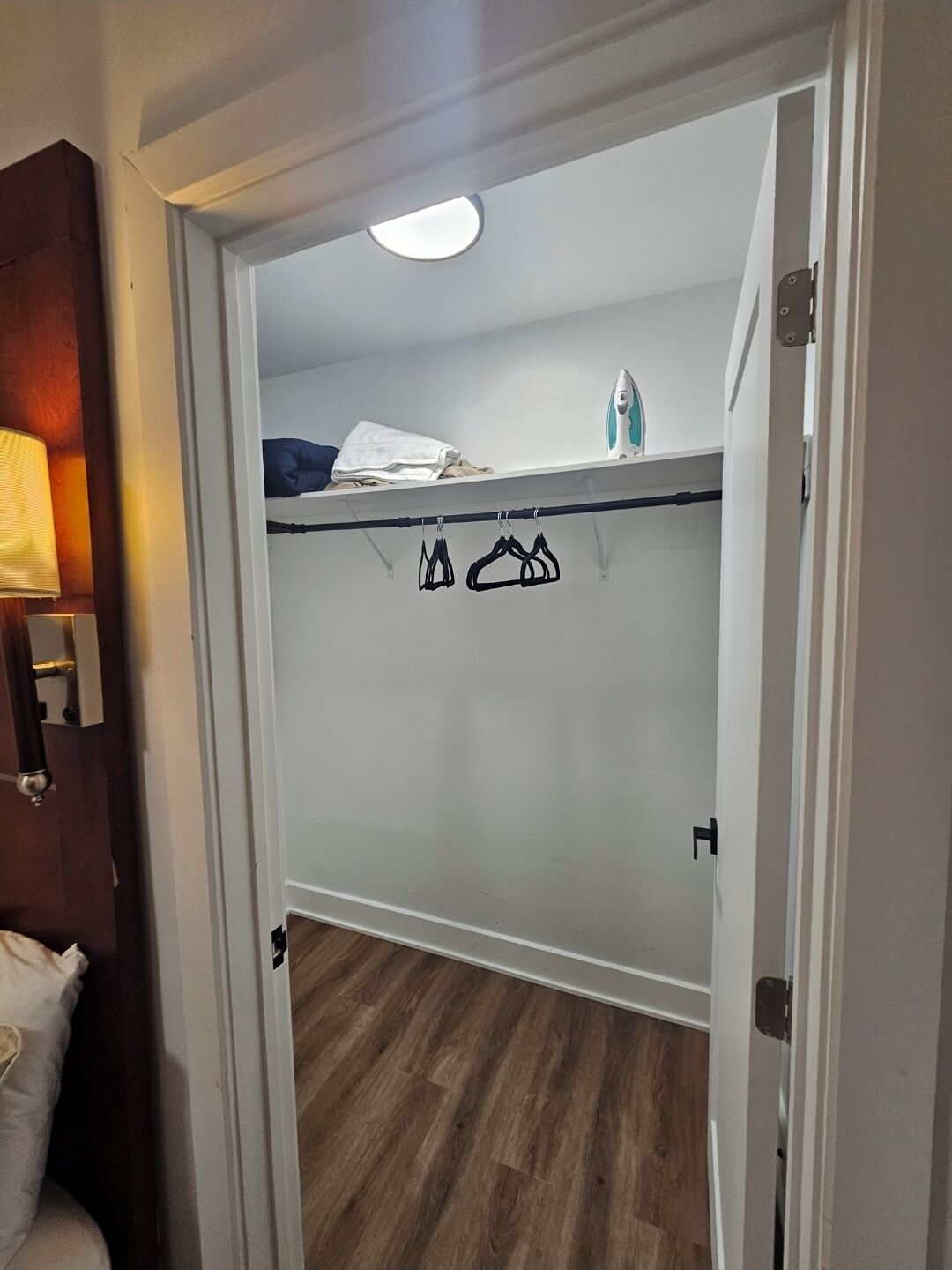 Un dressing accessible sans porte, avec un plancher en bois, une tringle à vêtements et un luminaire au plafond.