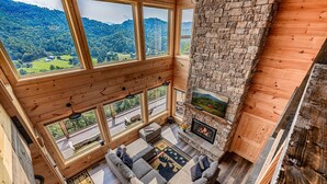 Ein Zimmer mit hohen Decken, großen Fenstern, einem steinernen Kamin und einer gemütlichen Sitzecke.