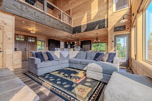 A spacious living room with a large sectional sofa, a wooden ceiling, and a view of the outdoors. - Cabin with Breathtaking Views, Hot Tub & Game Room (Sevierville)