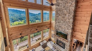 Ein Zimmer mit hohen Decken und großen Fenstern, das einen Blick auf eine bewaldete Landschaft bietet.