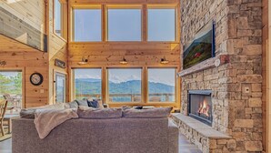 Ein gemütliches Wohnzimmer mit einer großen Couch, einem Kamin aus Stein und großen Fenstern mit Blick auf die Berge.
