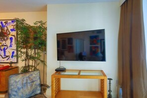 A living room with a flat-screen TV mounted on the wall, a wooden TV stand, a chair, a large potted plant, and a painting on the wall. - Suarez Art Stay, Scenic Miami View, Gym, Park (Miami)