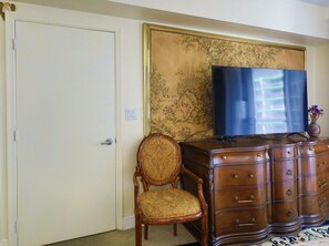 Een kamer met een gesloten deur, een houten stoel, een dressoir met lades, en een flatscreen televisie erboven.