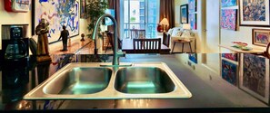Een moderne keuken met een dubbele spoelbak, een koffieapparaat en een eethoek met een tafel en stoelen.