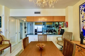A dining area with a wooden table and chairs, a chandelier, and a kitchen with modern appliances in the background. - Suarez Art Stay, Scenic Miami View, Gym, Park (Miami)