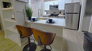 Una cocina moderna con armarios blancos, electrodomésticos de acero inoxidable, un lavabo y dos taburetes de madera.