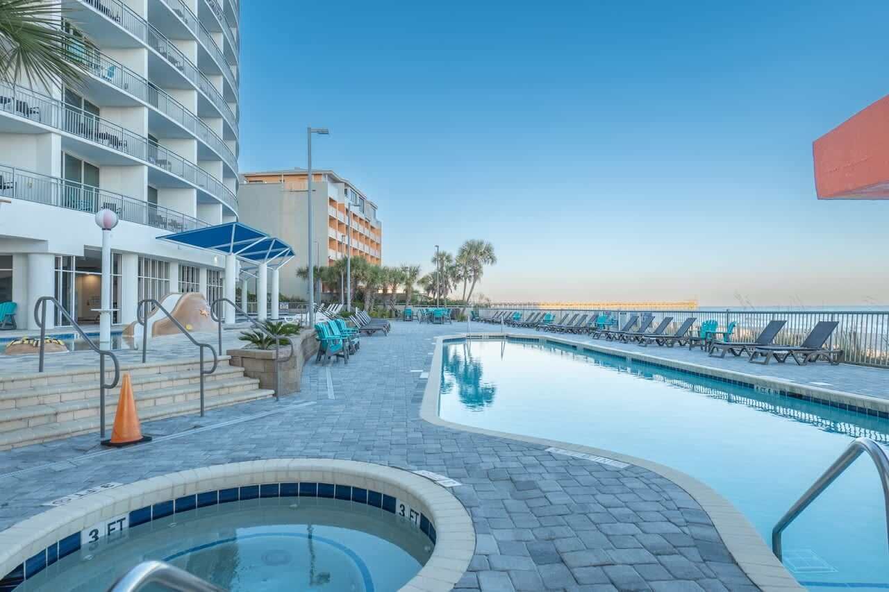 A pool area with a hot tub, lounge chairs, and a building with balconies.