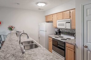 A kitchen with a granite countertop, stainless steel sink, white appliances, and wooden cabinets. - River Oaks 19-E (Myrtle Beach)