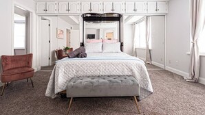 Ein Schlafzimmer mit einem großen Bett, einer grauen Bank, einem roten Sessel und weißen Schränken.